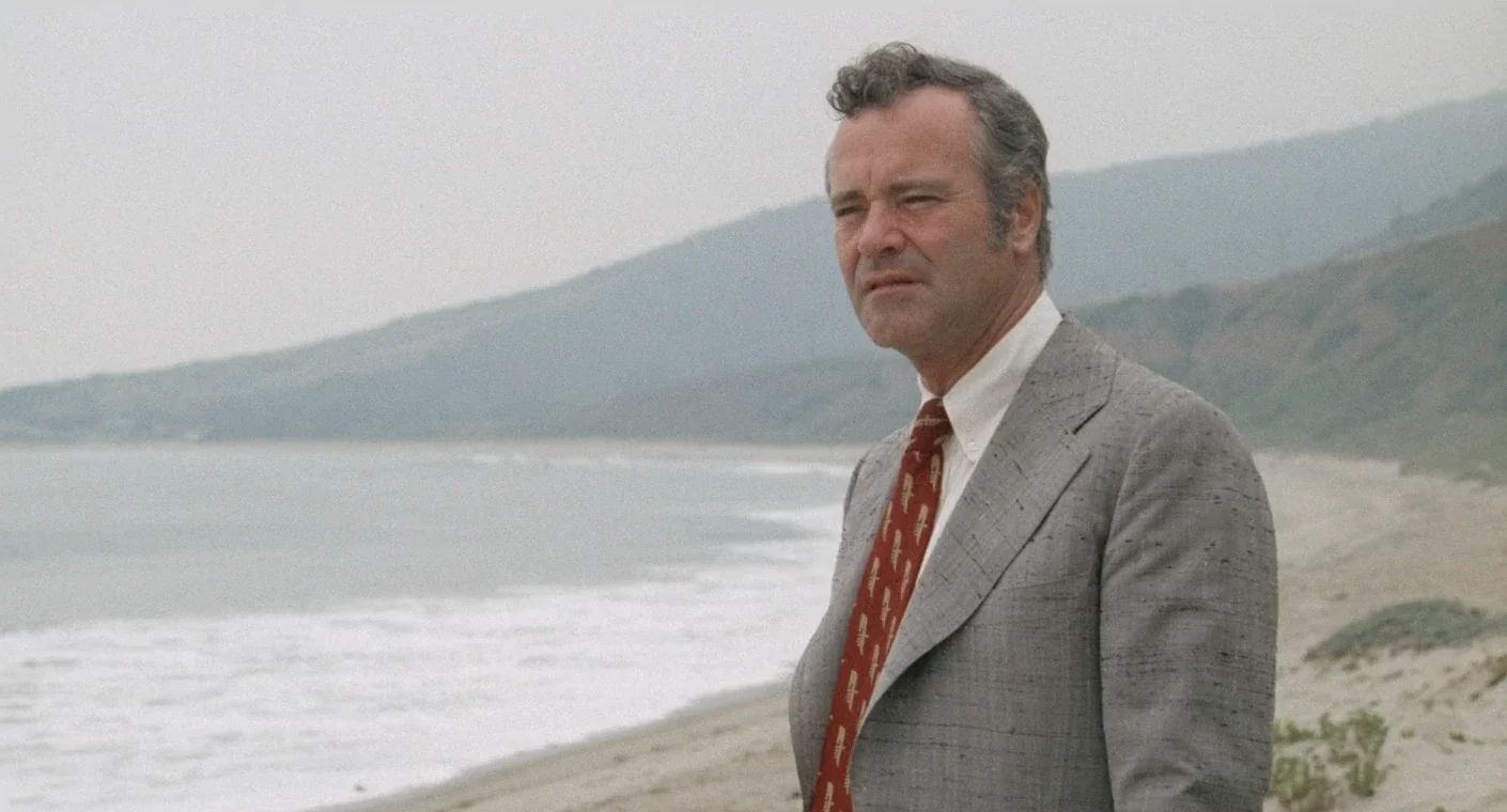 Why The 1972 Lincoln Continental Was The Perfect Movie Costar In This Jack Lemmon Drama 2 Movie screenshot of Jack Lemmon in a gray silk suit, standing on a Malibu beach looking morose