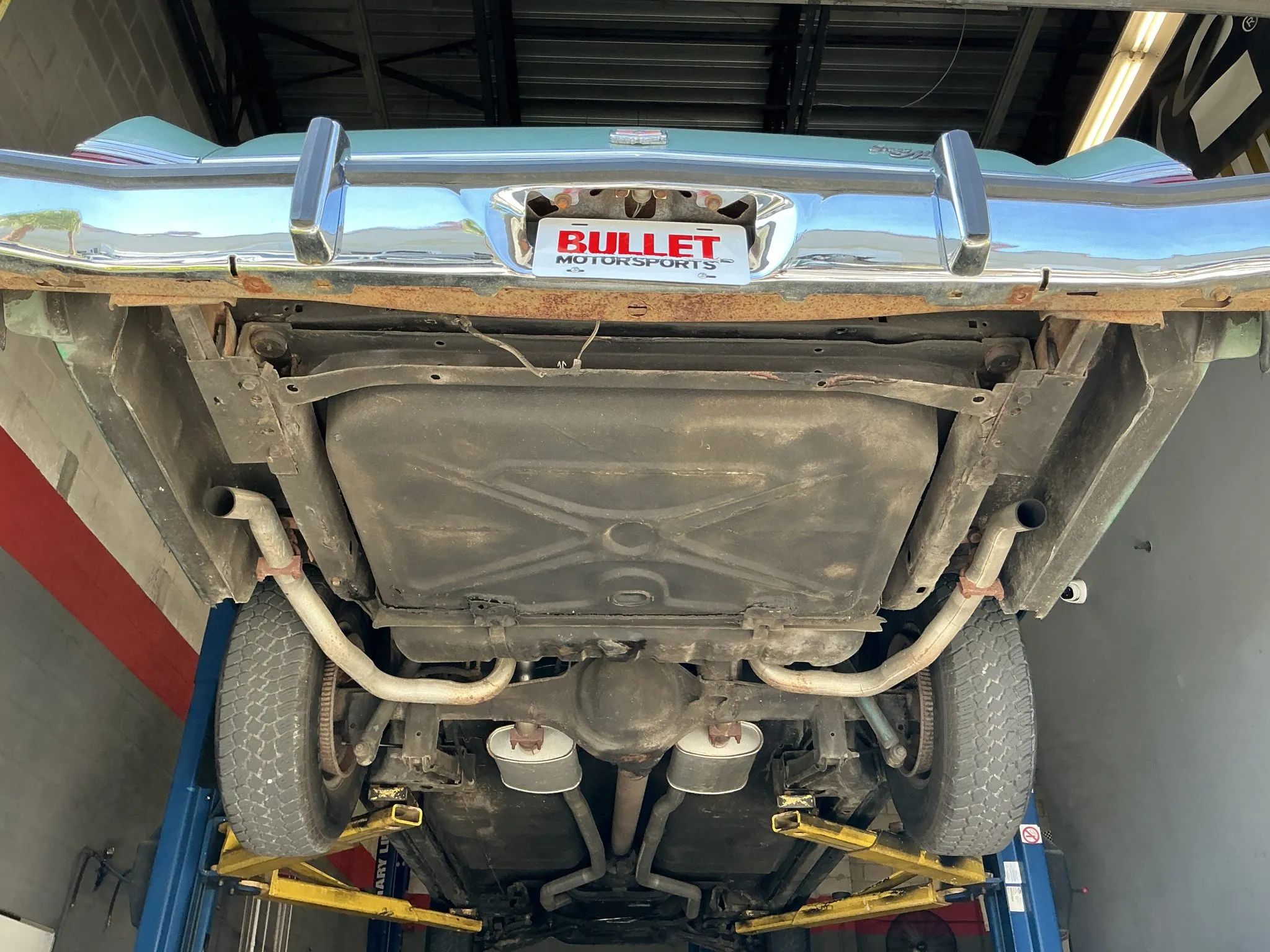 Fuel tank, mufflers, and rear axle under a 1977 Grand Marquis that's raised on a hoist