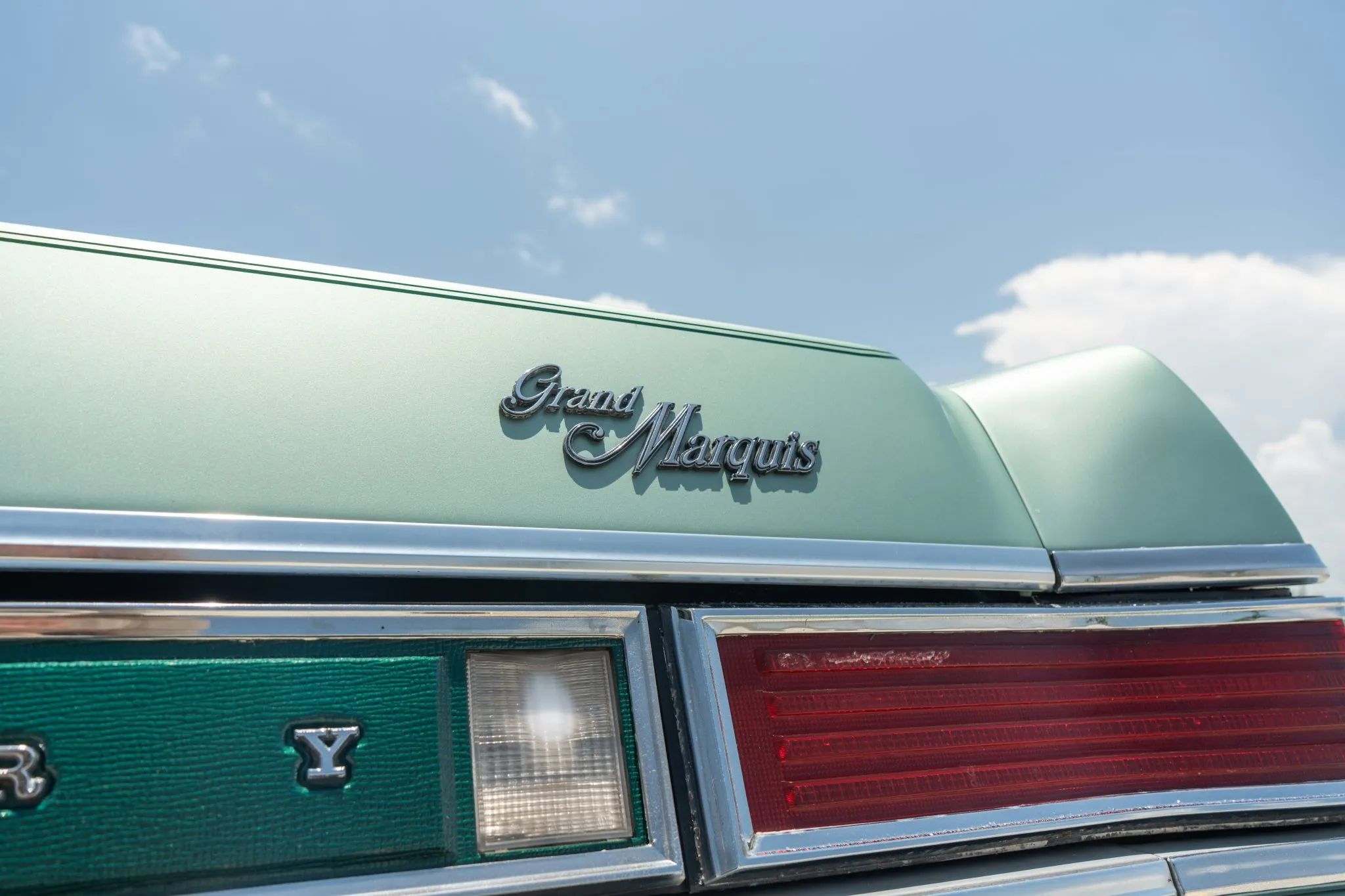 Closeup of the decklid of a 1977 Grand Marquis, with a script badge on the lid and a green vinyl panel between the backup lamps