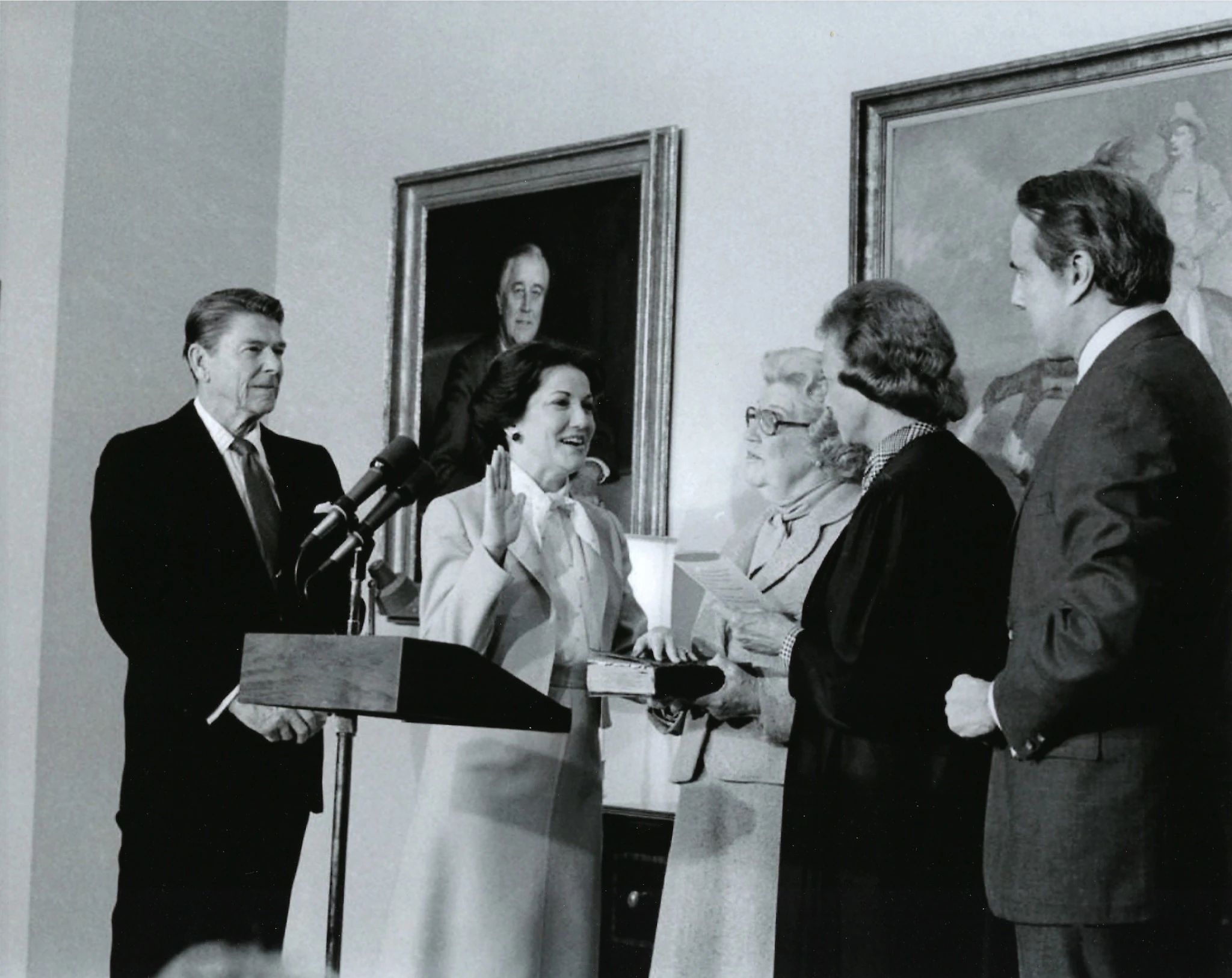 Elizabeth Dole with her hand up, being sworn in by Sandra Day O'Connor, with Ronald Reagan looming behind her
