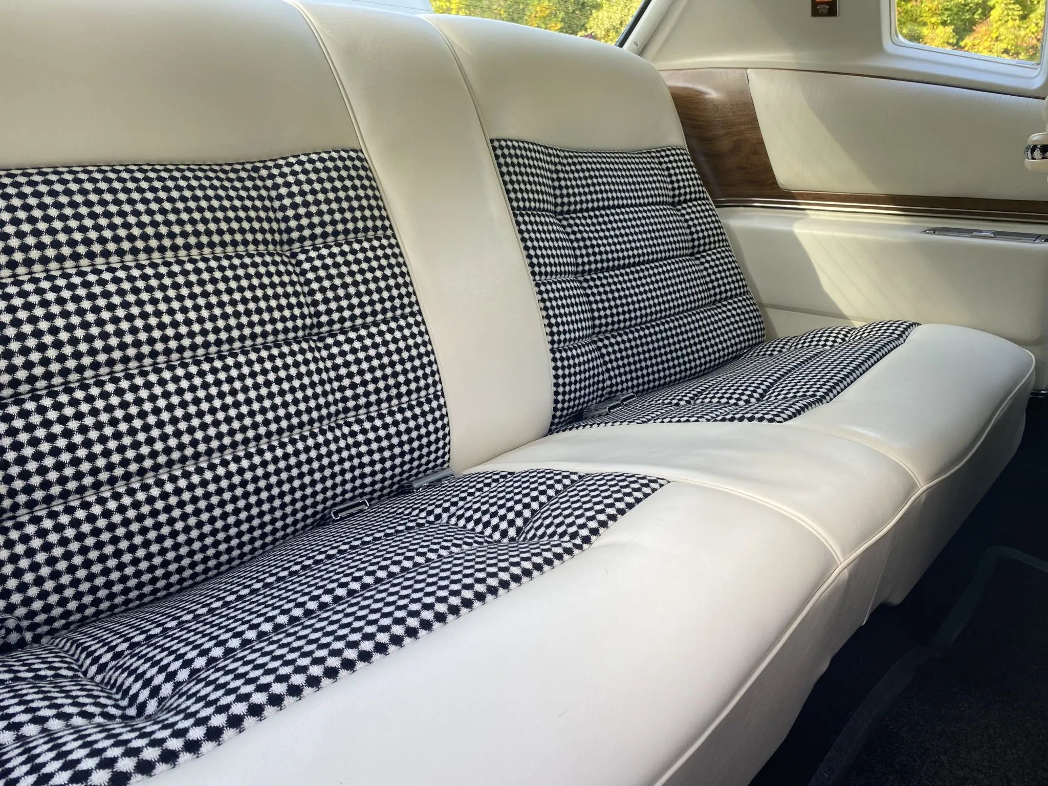 Back seat of a 1975 Cadillac Eldorado with white leather upholstery and black-and-white check pattern cloth inserts