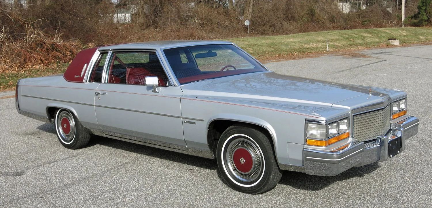 Right front 3q view of a silver 1981 Cadillac with a plum-colored vinyl half-top and matching wheel covers