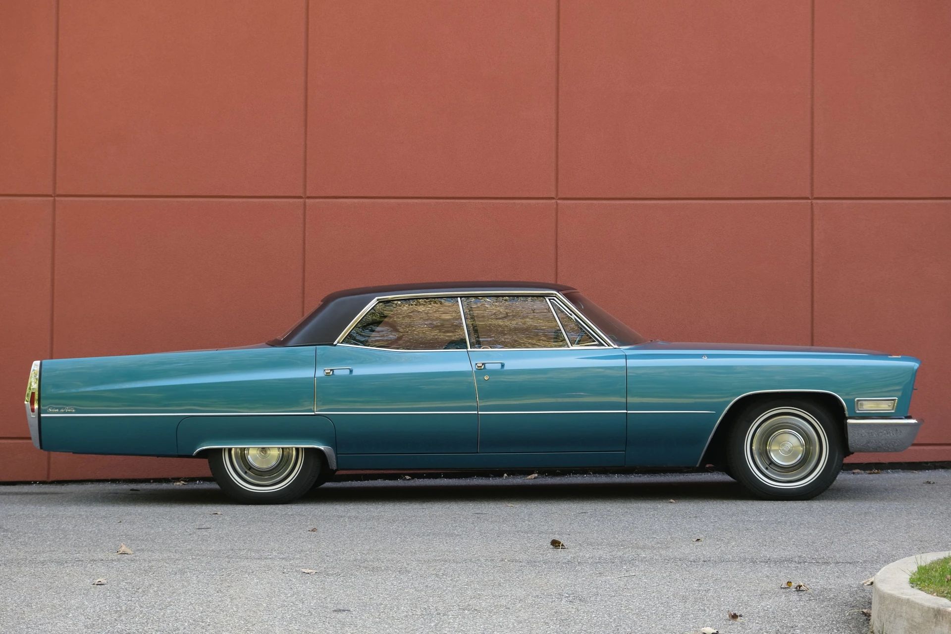 Right side view of a Caribe Aqua 1968 Cadillac Hardtop Sedan de Ville against a red wall