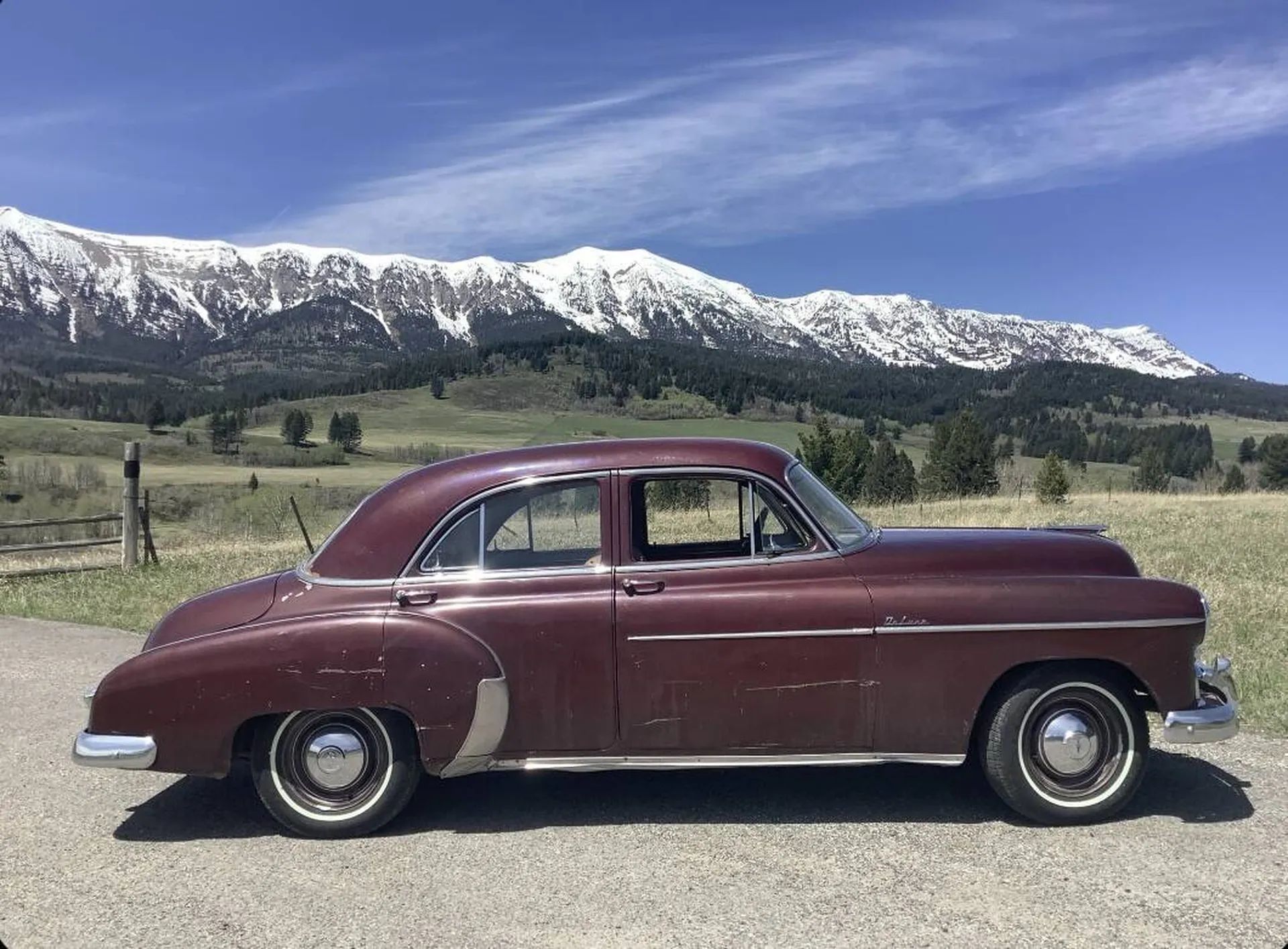 Passenger side profile picture of maroon 1949 Chevrolet sedan in front of a picturesque mountain range