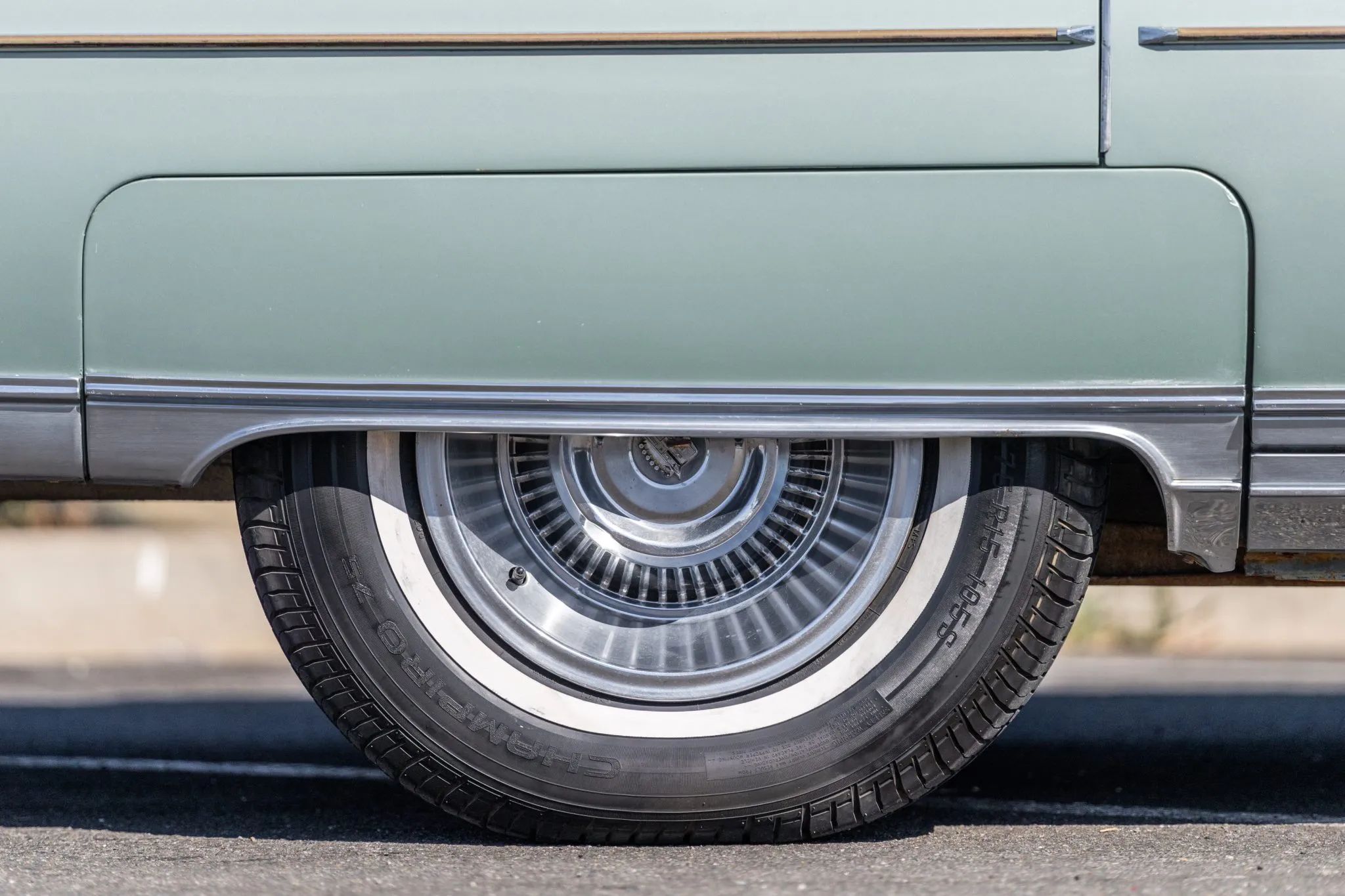 Closeup of the fender skirt of a green Cadillac with a band of chrome trim along the lower edge