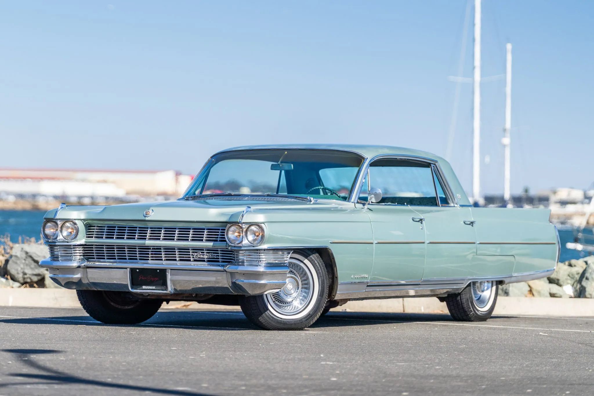 Left front 3q view of a 1964 Cadillac four-door hardtop parked in front of a harbor