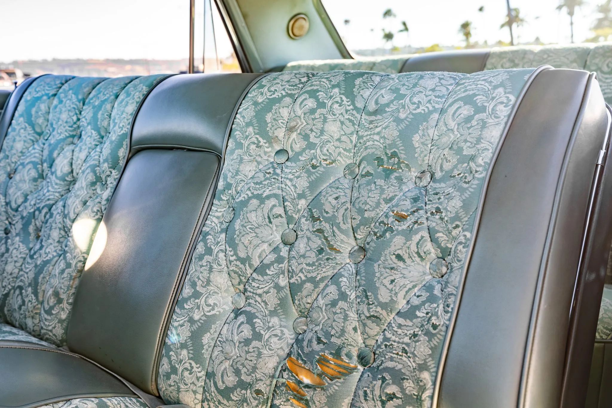Driver's side of the front seat of a 1964 Cadillac, with some tears in the floral print upholstery