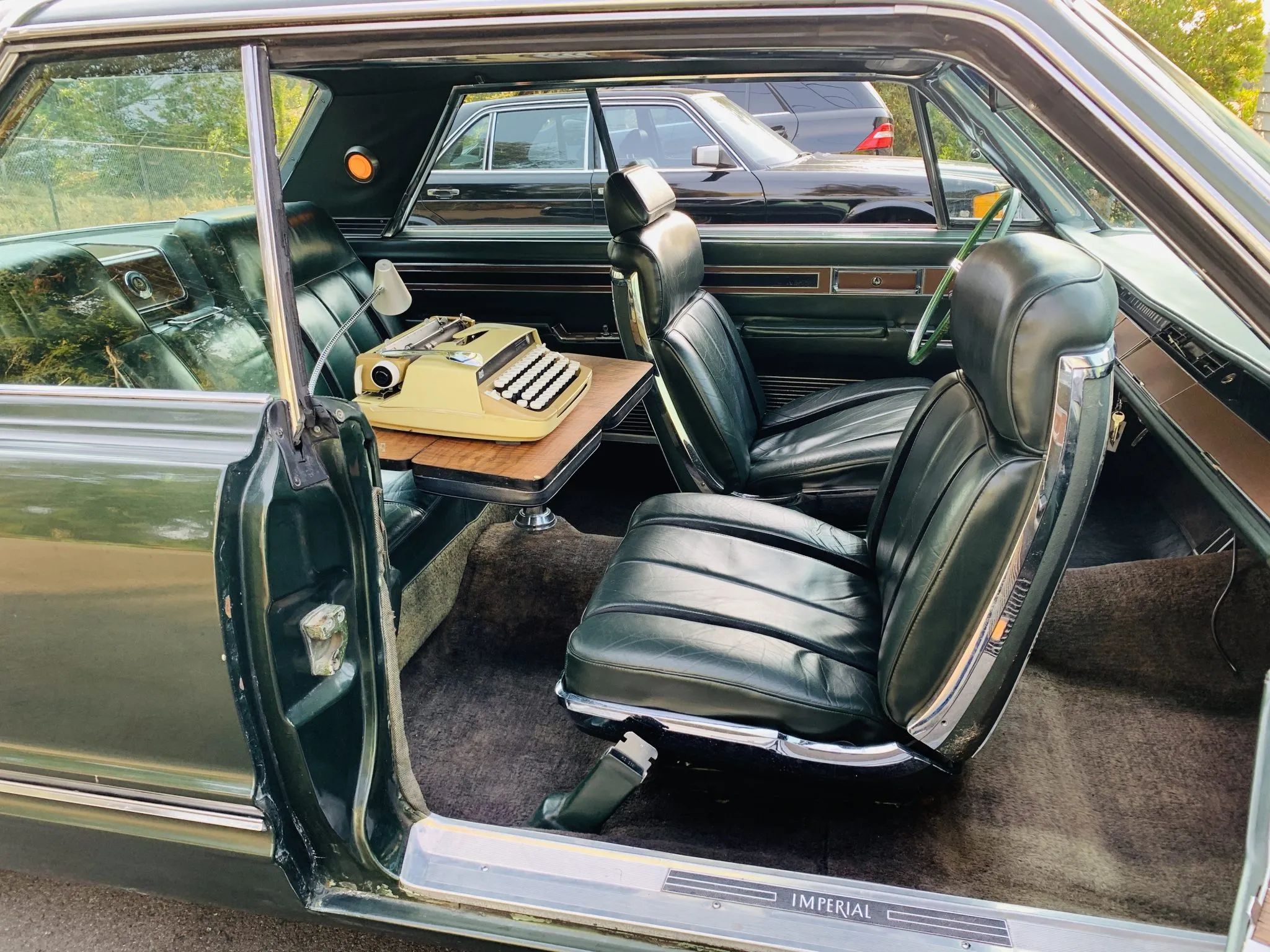 Back seat of a 1967 Imperial two-door hardtop with swiveling right front bucket seat and folding desk with a typewriter