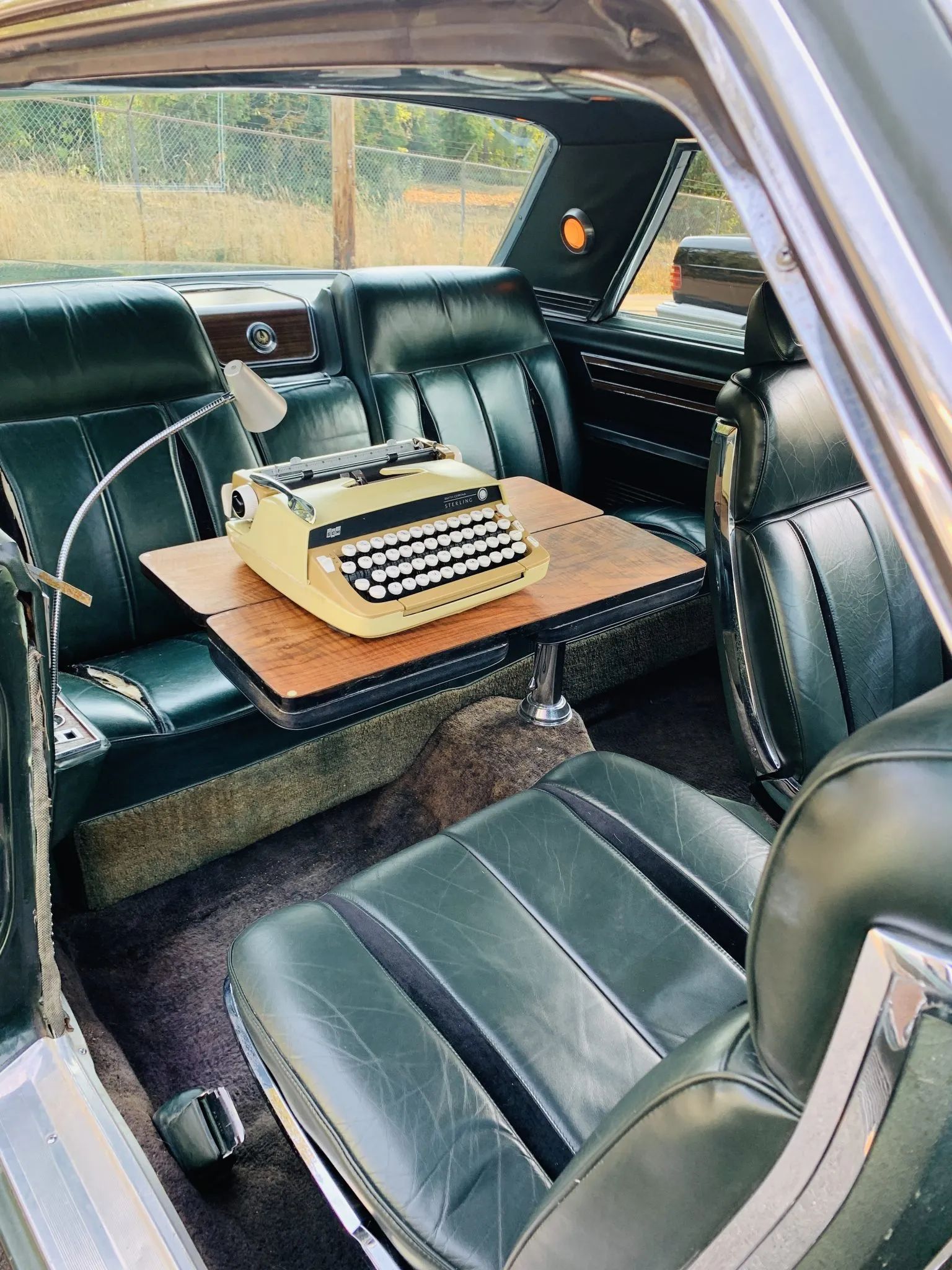 Rear seating area of a 1967 Imperial two-door hardtop with a lamp and a folding desk with a typewriter in the back seat