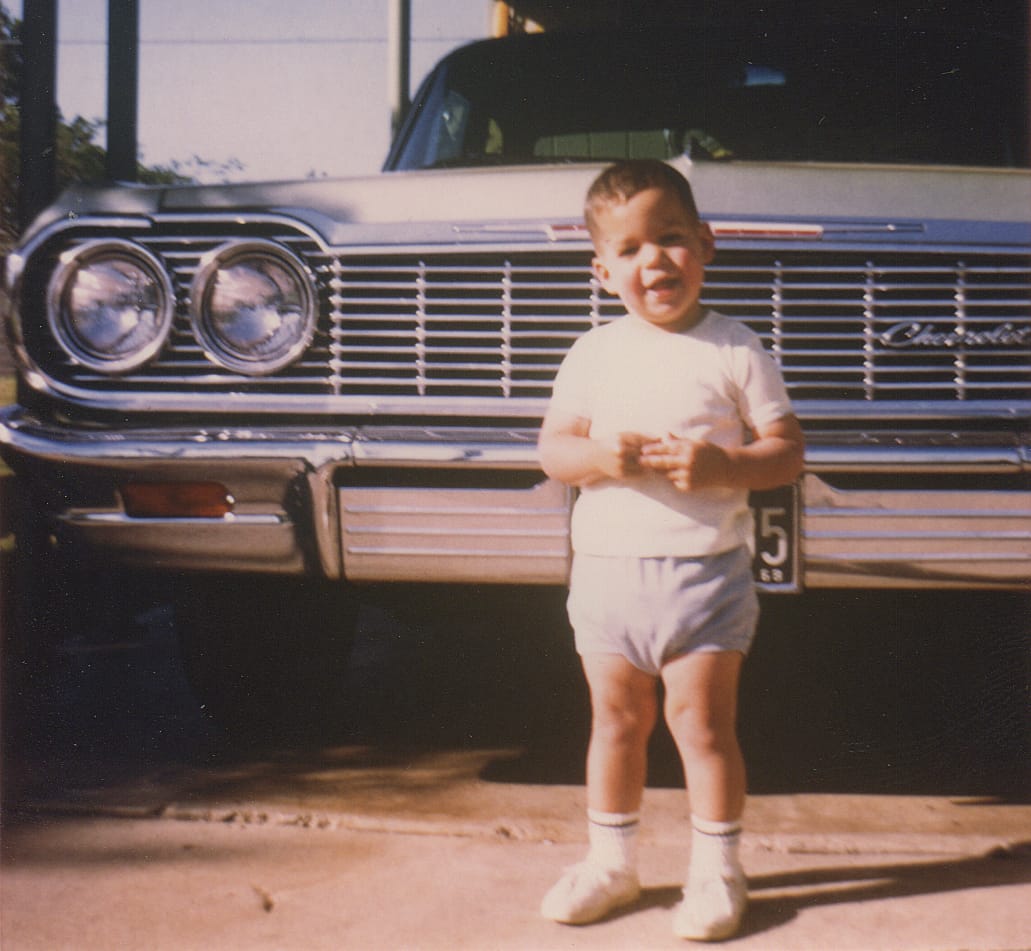Young boy standing in front of a 1964 Chevrolet Impala circa 1968