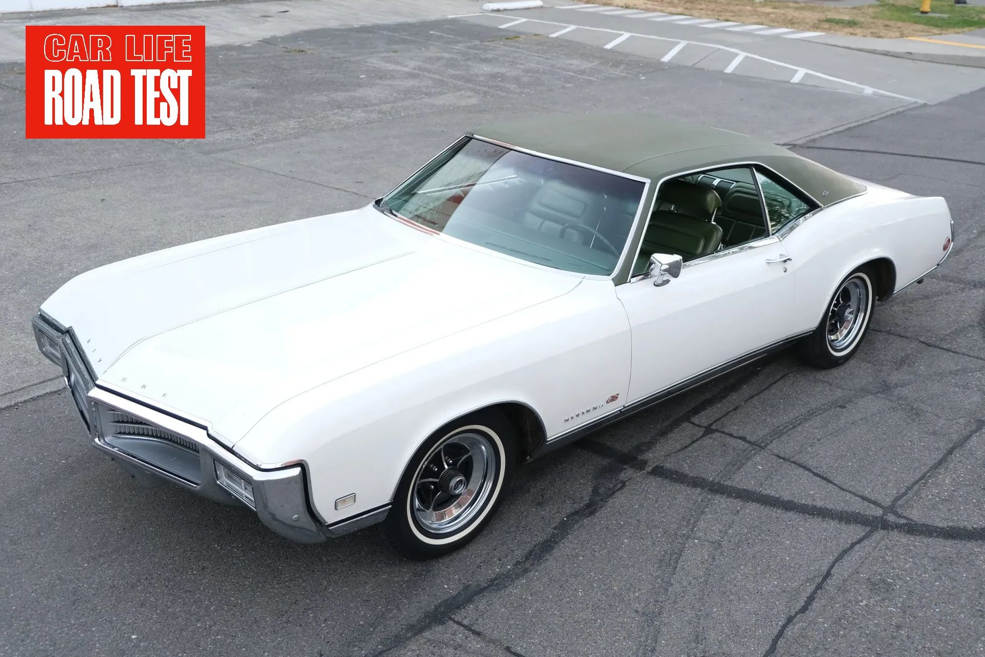 Vintage Car Life Review: 1969 Buick Riviera With Accu-Drive – Buick Tries Something New In The Suspension Department 1 Photo of a white 1969 Buick Riviera GS with a green vinyl top, seen from a high front 3q angle. An inset says "CAR LIFE ROAD TEST" in red and white
