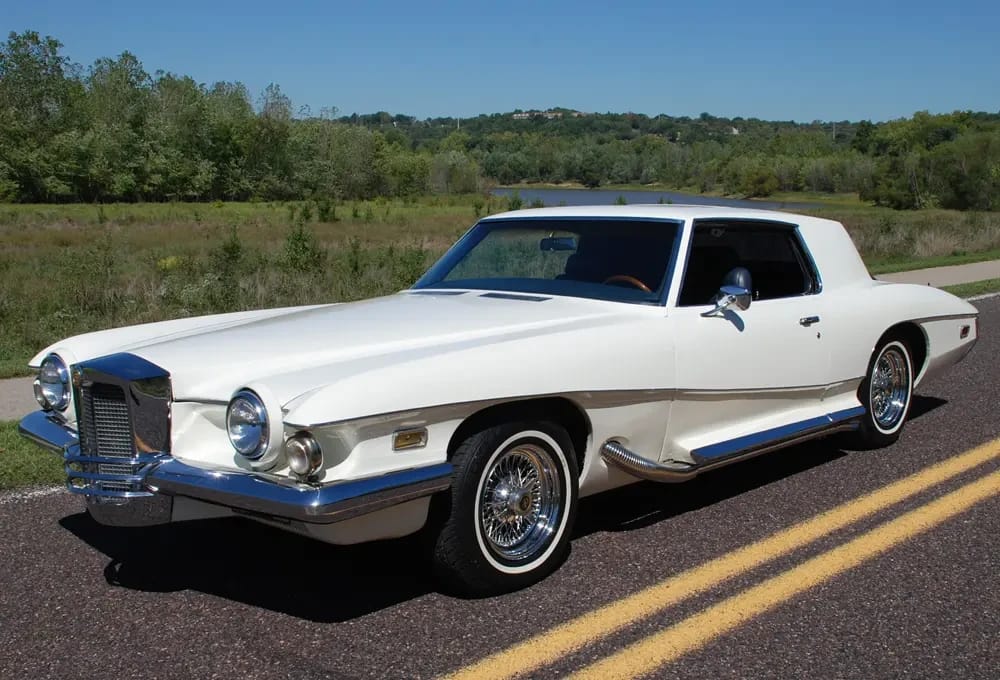 Left front 3q view of a white Stutz on a divided highway; the car now has a conventional one-piece windshield