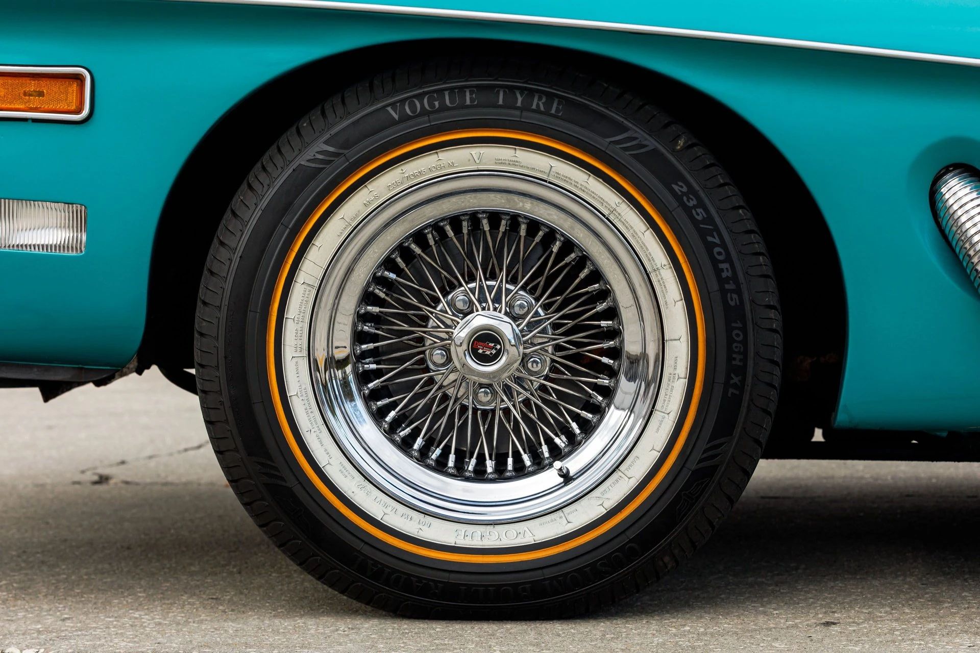 Closeup of a wire wheel with a tire with both white and gold stripes