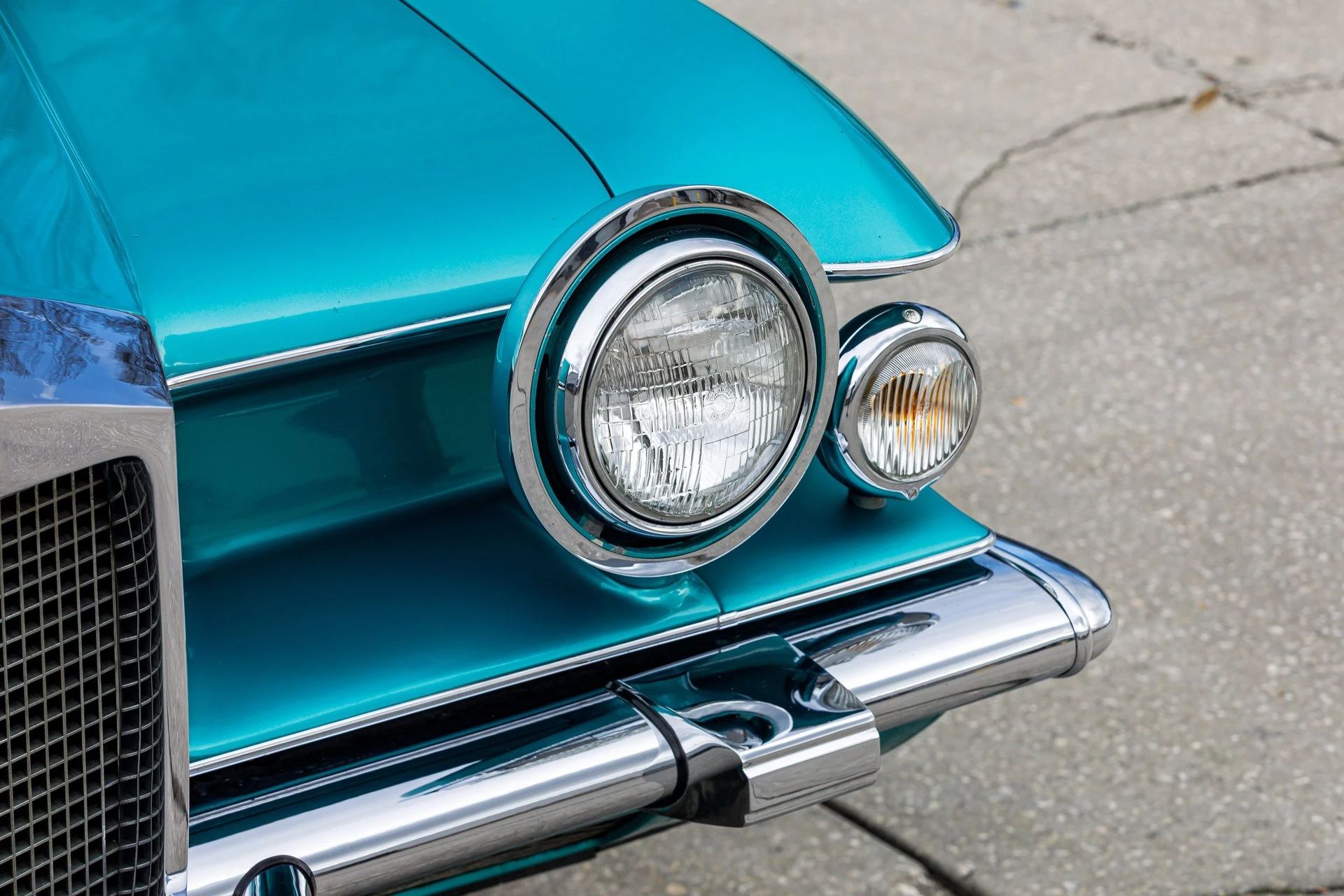 Closeup of the left headlight and running light of a turquoise Stutz