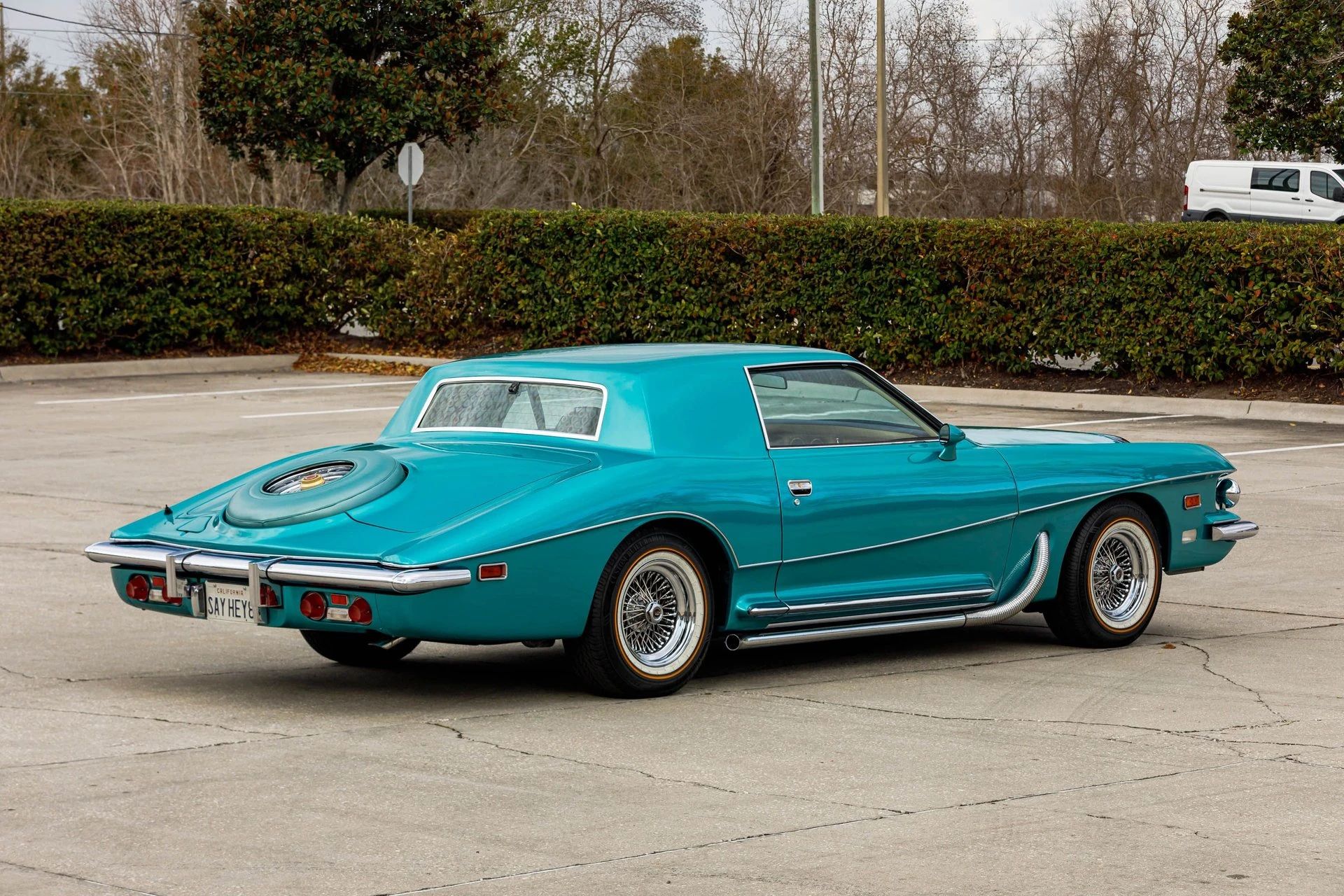 Rear 3q view of a turquoise coupe with the spare tire set into a body-colored hump on the rear deck