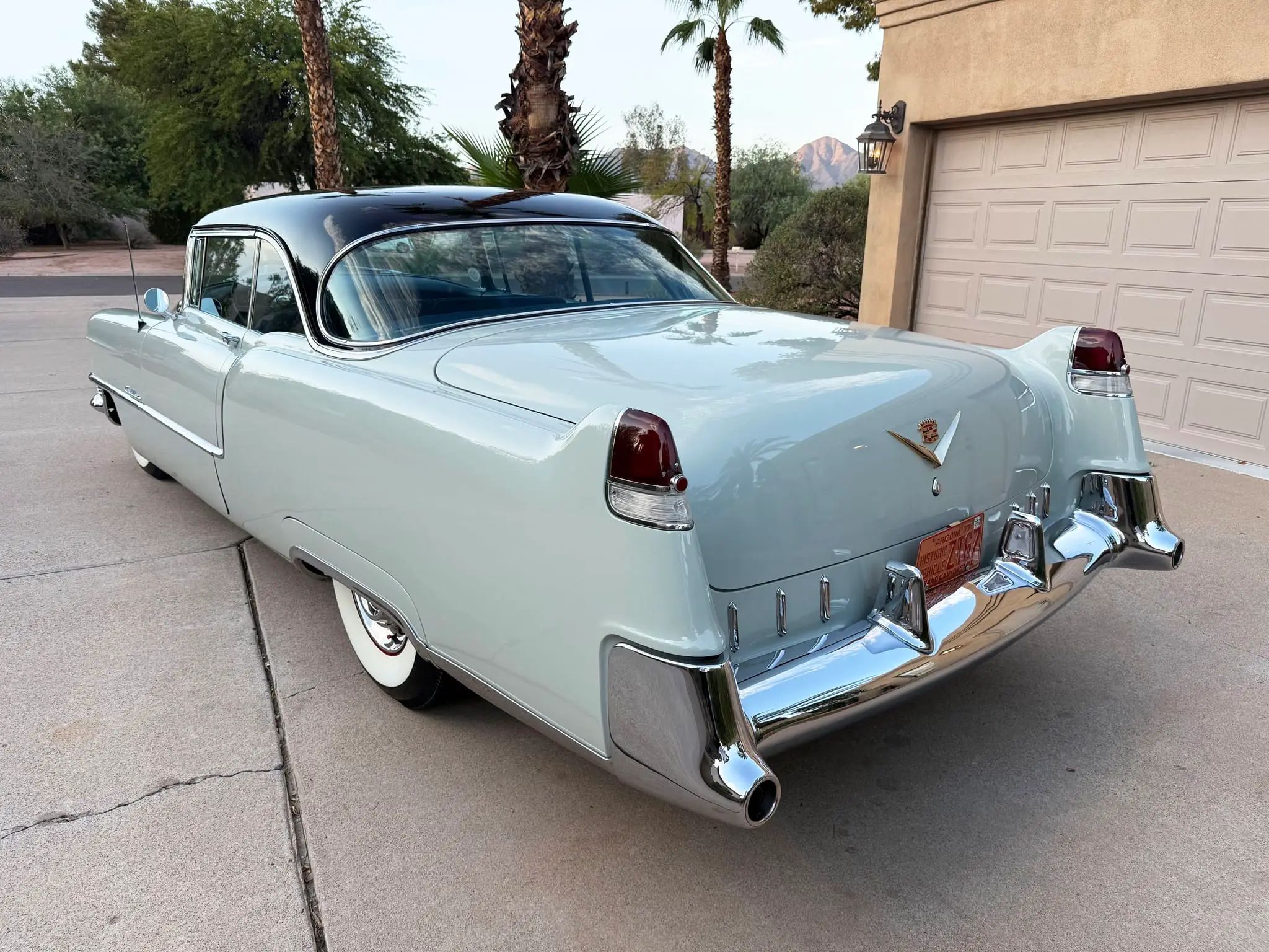 Driver rear 3q picture of gray 1955 Cadillac Series 62 Coupe parked in a driveway in front of a tan garage