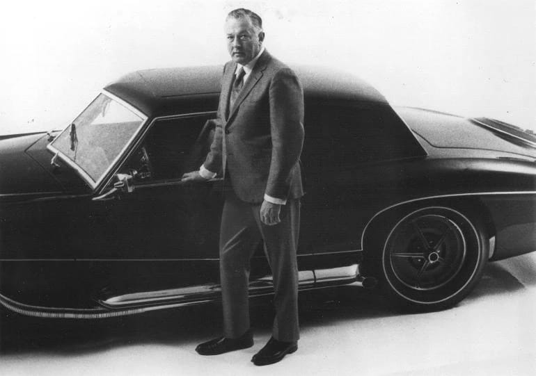 B&W photo of a man in a suit standing by an neoclassical coupe