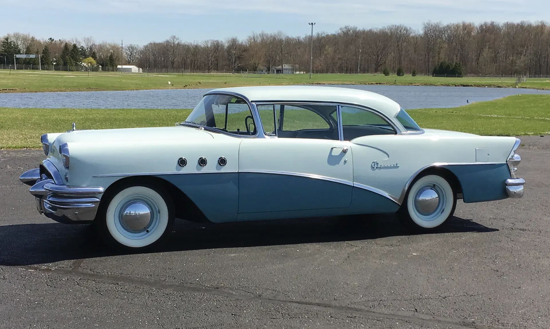 Left side view of a two-tone Buick two-door hardtop parked in front of a lake