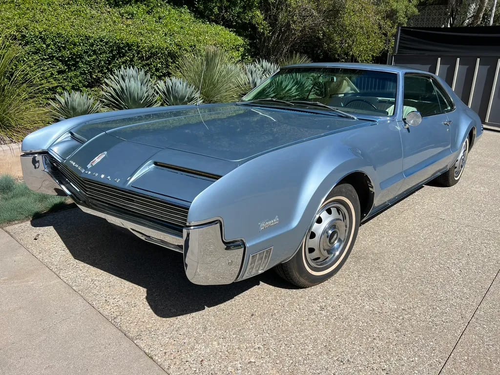 Riviera, Thunderbird, Eldorado, Toronado, Or GT Hawk: Which 1960s Personal Luxury Coupe Is *Your* Favorite? 9 Driver front 3q picture of blue 1966 Oldsmobile Toronado parked in front of shrubbery