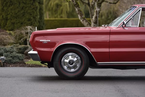 Front end of a Bright Red 1967 Plymouth GTX hardtop with 14-inch wheels and Deluxe wheel covers
