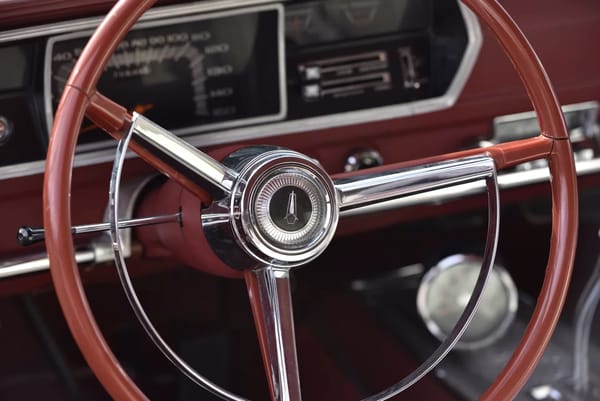 Steering wheel of a 1967 Plymouth GTX with red interior and a tachometer on the center console