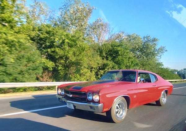 In Motion Classic: 1970 Chevrolet Chevelle SS In Hungary 1 Left front 3q view of a red 1970 Chevrolet Chevelle SS with black stripes on the hood, photographed on a highway with trees in the background