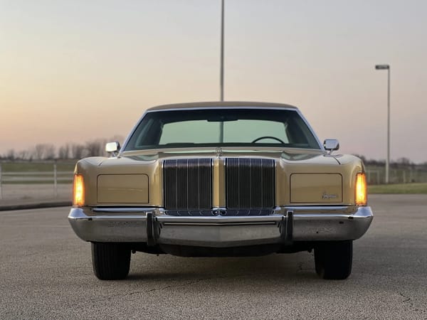 Front view of a gold 1974 Imperial LeBaron Crown Coupe, photographed at sunset with the parking lights on